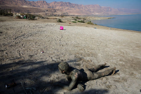 A man covered with mud from the Dead Sea lies down on the shore of the Dead Sea, near Metzoke Dragot in the Israeli occupied West Bank, January 9, 2018. REUTERS/Ronen Zvulun