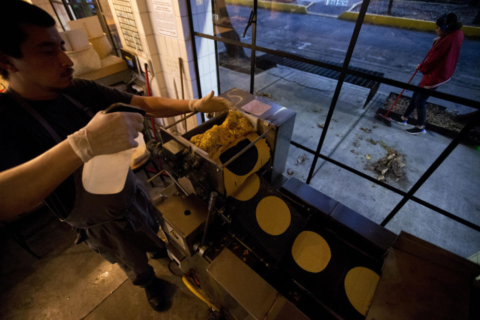 Chef Jesus Saldivar feeds ground corn through the tortilla making machine at El Pujol Mill in the Condesa neighborhood of Mexico City, Tuesday, April 9, 2019. The shop is part of a new tortilla movement launched by a handful of chefs, restaurants and organizations to restore and popularize authentic tortillas, made of only corn, water and lime or calcium carbonate. (AP Photo/Rebecca Blackwell)