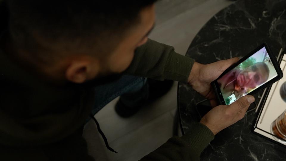 Jawdat Mikhael holds his phone while he speaks with his father, on videocall