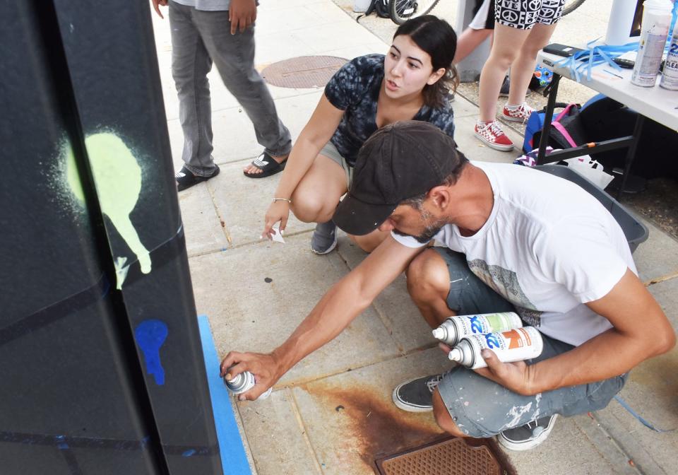 YEAH Corps youth mentor Sara Martins and artistic director Fernando Pezzino work on the electric box at the Fall River Justice Center.