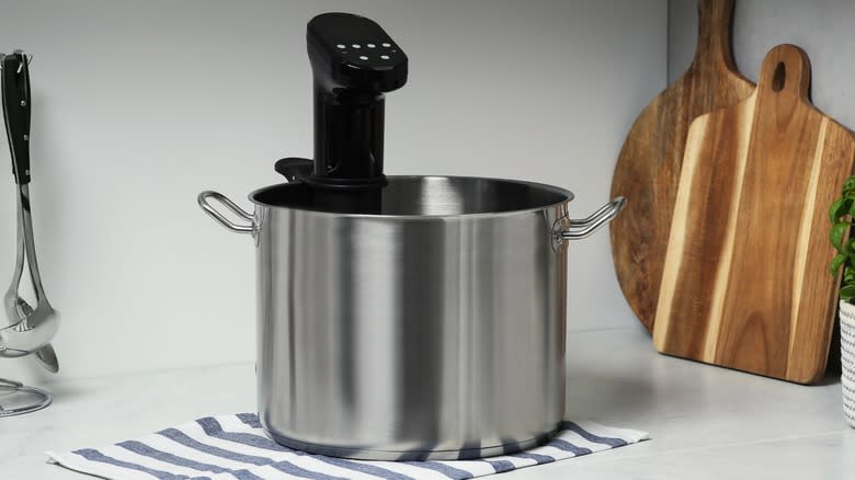 Sous vide machine attached to a silver pot on a kitchen counter