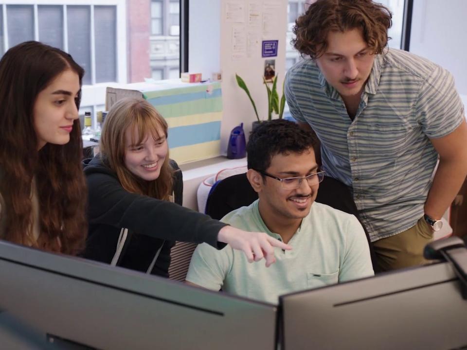 Four D. E. Shaw interns gathered around a computer.