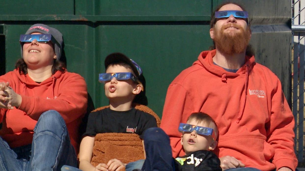 A family in Florenceville-Bristol on Monday watch the eclipse in its partial phase using eclipse glasses. Some people across the province are now collecting the glasses for reuse. (Ed Hunter/CBC - image credit)