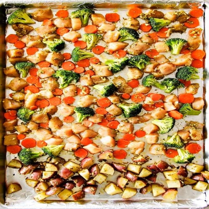 Diced raw chicken, potatoes, tomatoes, and broccoli on a baking sheet