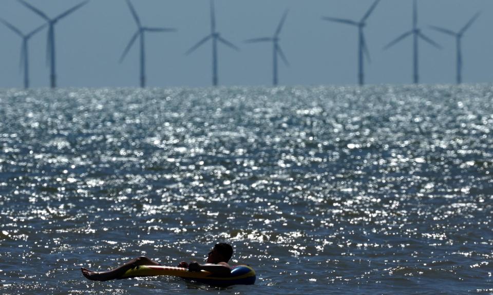 <span>Fixed and floating: a swimmer relaxes within sight of a conventional offshore wind installation off Walton-on-the-Naze in Essex.</span><span>Photograph: Toby Melville/Reuters</span>