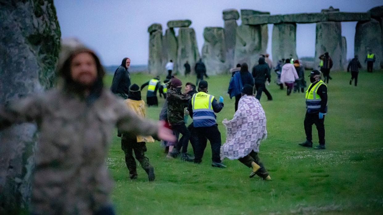 Menschen springen über einen Zaun und bahnen sich ihren Weg an Sicherheitspersonal vorbei in Richtung Stonehenge.