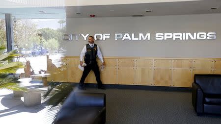 An investigator walks through the lobby of Palm Springs City Hall while news media are reflected on glass during a raid on the city's offices in Palm Springs, California, September 1, 2015. REUTERS/Sam Mircovich