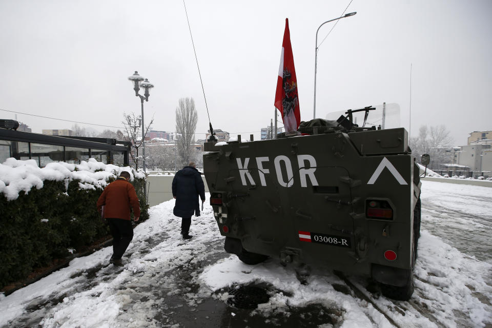 People pass by a NATO-led peacekeeping force KFOR vehicle in front of the main bridge between the southern, ethnic Albanian-dominated and the northern, Serb-dominated part of Mitrovica, Kosovo, Friday, Dec. 14, 2018. Kosovo's parliament overwhelmingly approved the formation of an army, a move that has angered Serbia which says it would threaten peace in the war-scarred region. (AP Photo/Darko Vojinovic)