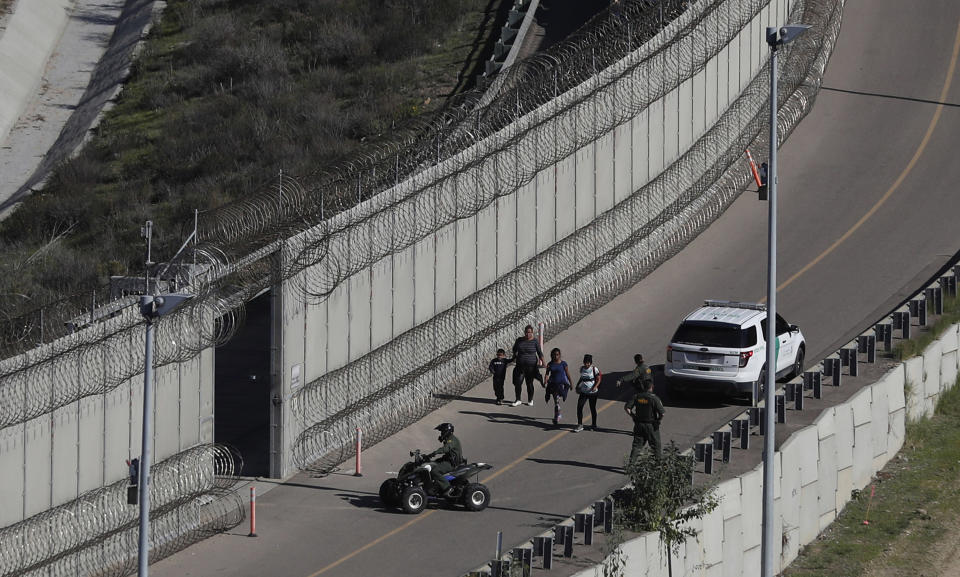 FILE - In this Dec. 16, 2018, file photo, Honduran asylum seekers are taken into custody by U.S. Border Patrol agents after the group crossed the U.S. border wall into San Diego, in California, seen from Tijuana, Mexico. The state of California is freeing up to $28 million to help asylum-seekers released in the U.S. with notices to appear in court with hotels, medical screenings, and transportation. California's generosity is a stark contrast to Arizona and Texas, where border state officials have challenged and sharply criticized President Joe Biden's immigration policies. (AP Photo/Moises Castillo, File)