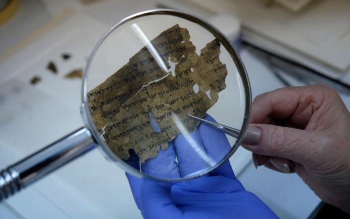 A worker of the Israeli Antiquity Authority sews fragments of the Dead Sea scrolls which includes biblical verses in a preservation laboratory of the Israel Museum in Jerusalem - Moment Mobile ED