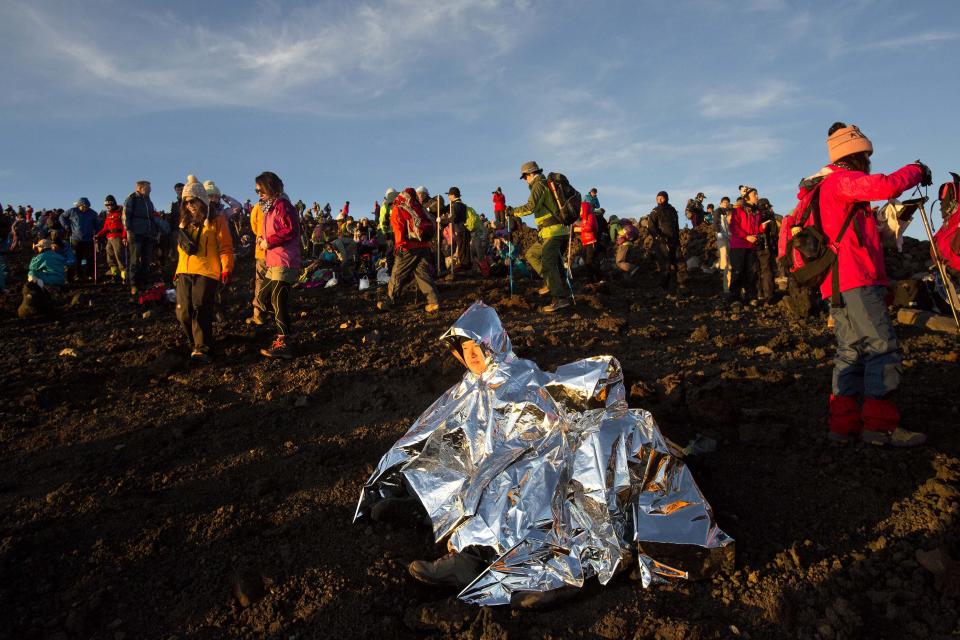 In this Sunday, Aug. 11, 2013 photo, a Japanese couple sits under a space blanket to keep warm on top of the the summit of Mount Fuji in Japan at dawn. The recent recognition of the 3,776-meter (12,388-foot) peak as a UNESCO World Heritage site has many here worried that will draw still more people, adding to the wear and tear on the environment from the more than 300,000 who already climb the mountain each year. (AP Photo/David Guttenfelder)