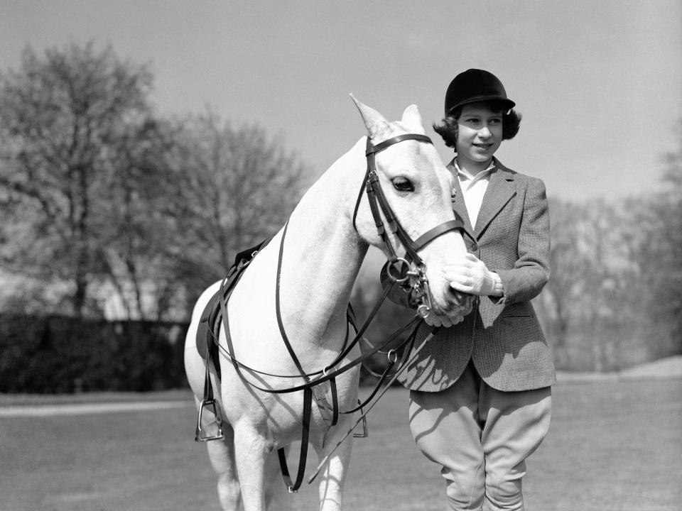 Queen Elizabeth wearing riding clothes posing with a horse in 1939.