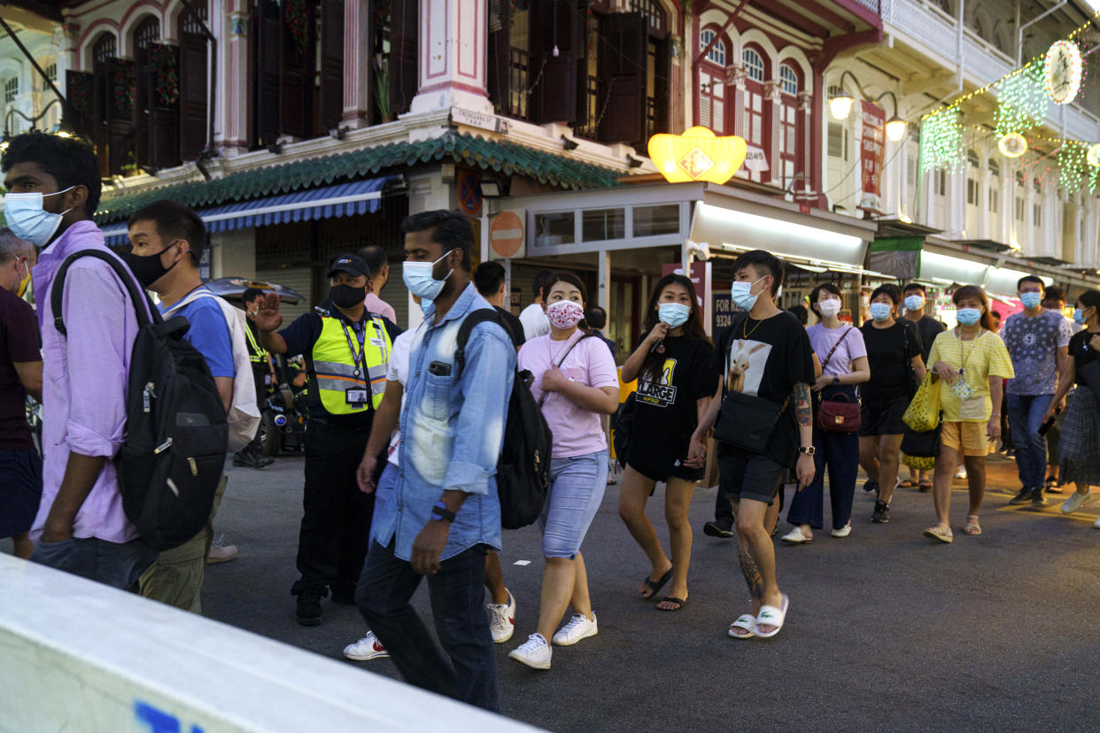 SINGAPORE, SINGAPORE - FEBRUARY 06: People crosses a road as security officers direct crowd traffic in Chinatown on February 6, 2021 in Singapore. The Chinese diaspora of Southeast Asia is celebrating a somewhat subdued Lunar New Year, as Covid-19 restrictions cut into what is traditionally a time for people to meet their relatives and take part in celebrations with extended families. In Singapore, where the spread of Covid-19 has been less extensive, each household will be permitted to have only up to 8 visitors per day, and authorities are encouraging the ethnic Chinese majority to visit no more than two households. (Photo by Ore Huiying/Getty Images)