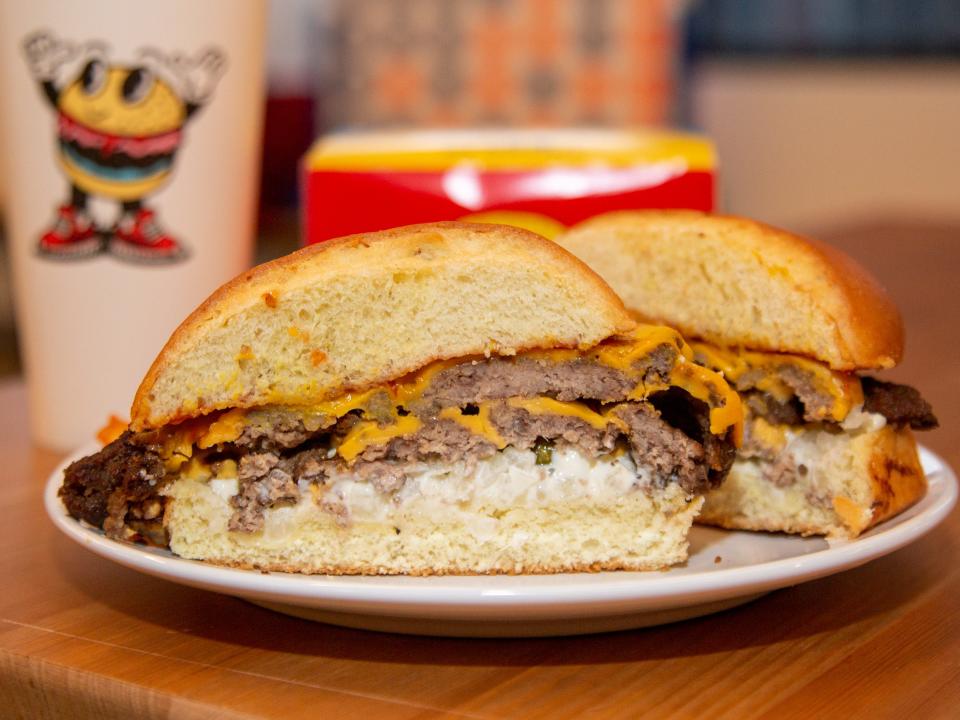 A burger on a paper box with a cup in the back.