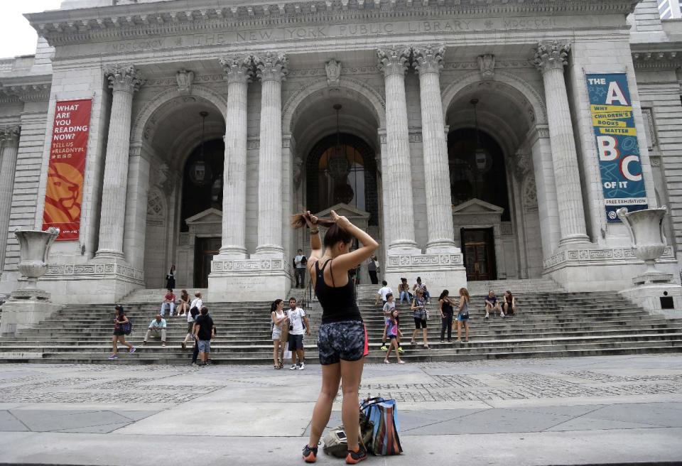 In this Monday, July 22, 2013 photo, a woman fixes her hair in front of the main branch of the New York Public Library in New York. Plans for a major change within the New York Public Library’s landmark main building have kindled an intellectual culture clash over its direction and the future of libraries themselves. (AP Photo/Seth Wenig)