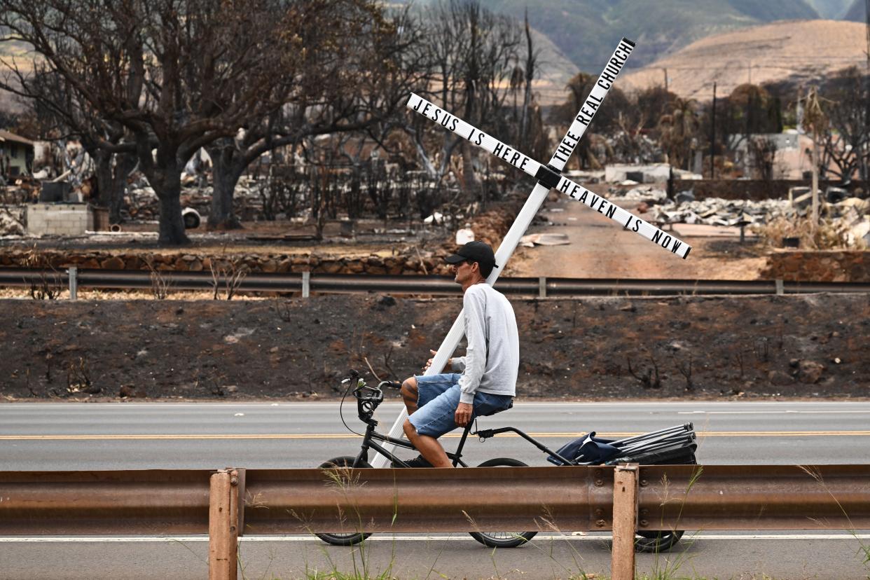 A man on a bike carries a cross in the north side of Lahaina, Hawaii (AFP/Getty)