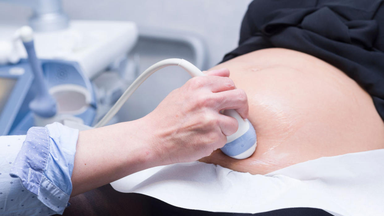  Close up on a health care provider's hand as she places an ultrasound device on a pregnant person's exposed stomach. 