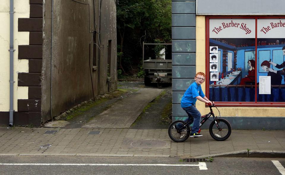 Boy rides his bicycle past an empty building which has been covered with artwork to make it look more appealing, in the village of Bushmills on the Causeway Coast