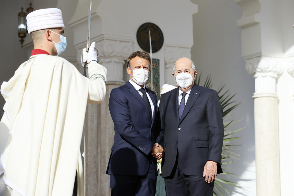 French President Emmanuel Macron, center, shakes hands with Algerian President Abdelmajid Tebboune, Thursday, Aug. 25, 2022 in Algiers. French President Emmanuel Macron is in Algeria for a three-day official visit aimed at addressing two major challenges: boosting future economic relations while seeking to heal wounds inherited from the colonial era, 60 years after the North African country won its independence from France. (AP Photo/Anis Belghoul)