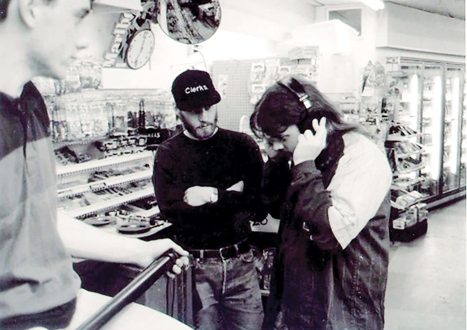 During the filming of 1994's "Clerks," director Kevin Smith, right, listens in on a pair of headphones while Vincent Pereira, left, holds the boom mike and Scott Mosier, center, can be seen in a "Clerks" cap.