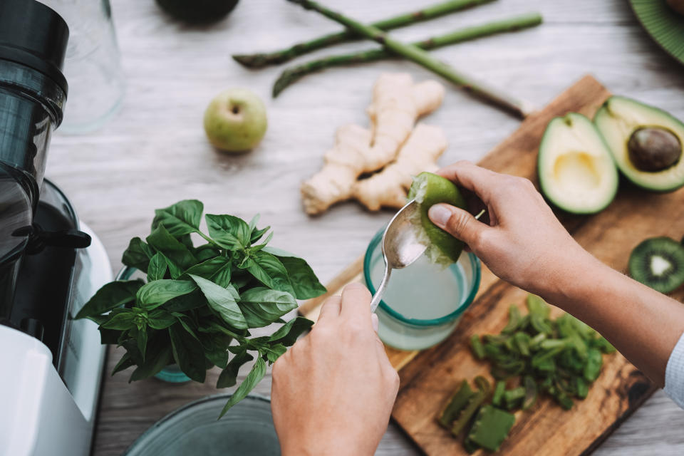 Young woman preparing detox juice with green vegetables and fruits - Focus on left hand