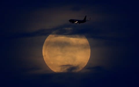A plane passes as the moon rises through clouds before start of total lunar eclipse in California - Credit: &nbsp;MIKE BLAKE/Reuters