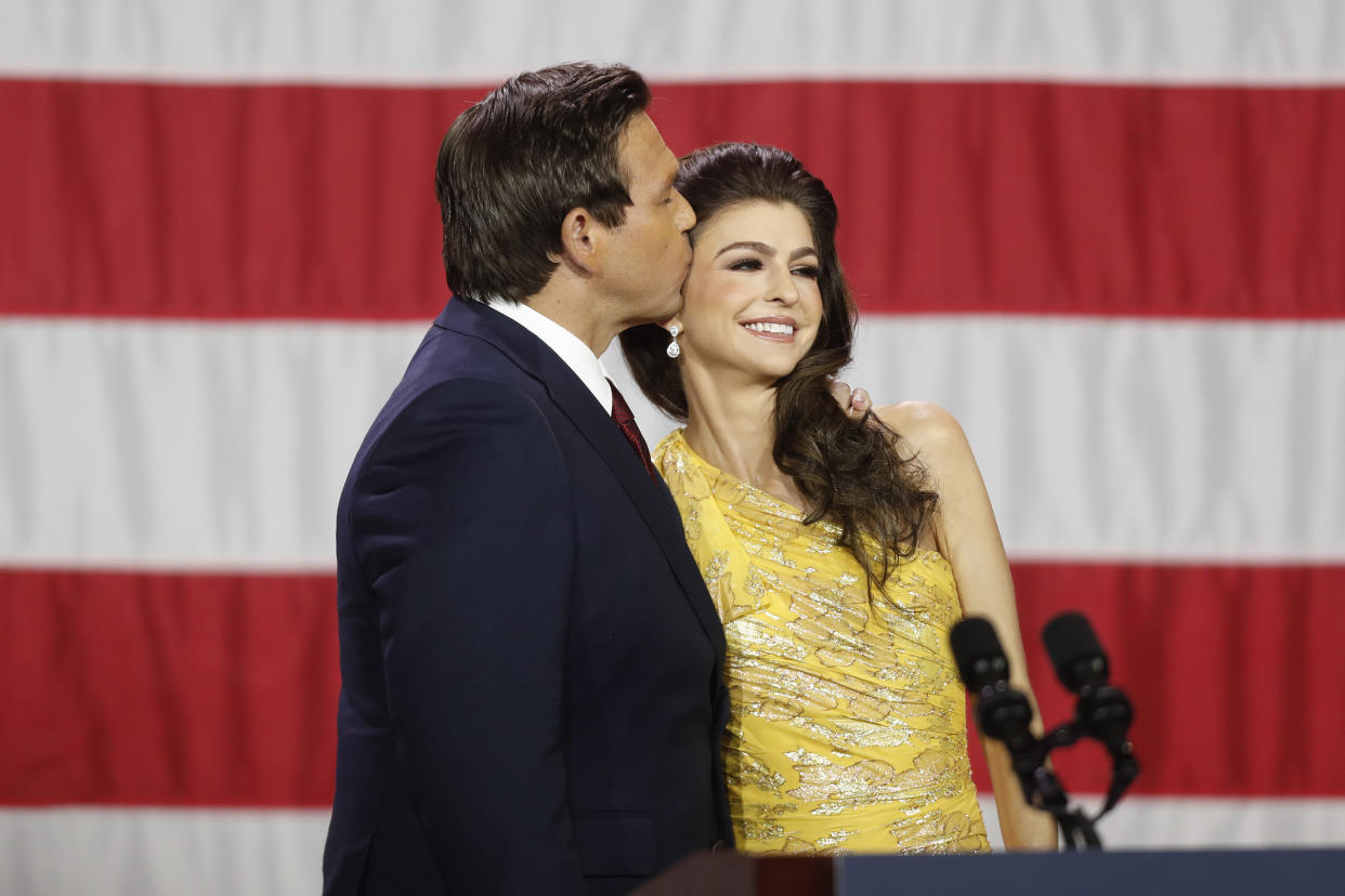 Gov. Ron DeSantis, on a stage, plants a heartfelt kiss on his wife, Casey, in yellow evening gown.