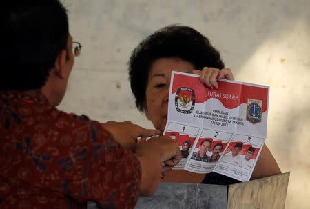 An election official assists an ethnic Chinese Indonesian woman before she casts her ballot during an election for Jakarta's governor, in Jakarta, Indonesia, February 15, 2017. REUTERS/Beawiharta