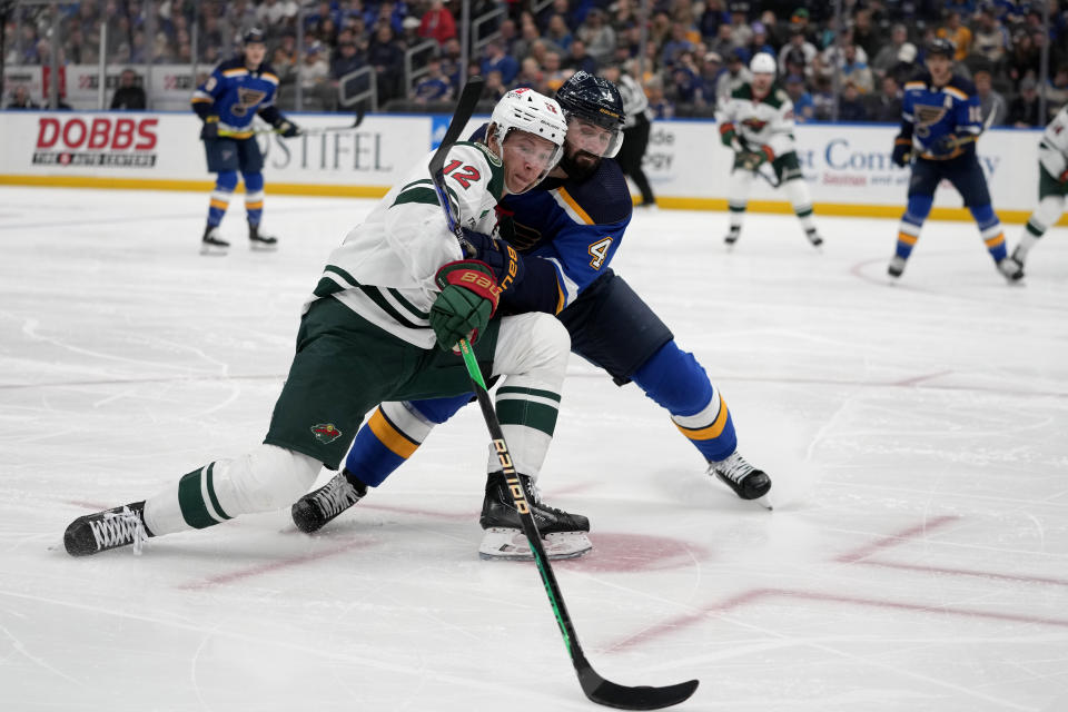 Minnesota Wild's Matt Boldy (12) and St. Louis Blues' Nick Leddy (4) battle for a loose puck during the first period of an NHL hockey game Wednesday, March 15, 2023, in St. Louis. (AP Photo/Jeff Roberson)