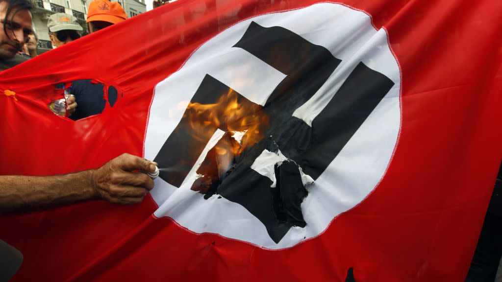 Demonstrators burn a flag emblazoned with a swastika during a demonstration against the visit of German Chancellor Angela Merkel in central Athens, October 9, 2012. Germany's Angela Merkel arrived in Greece on her first visit since Europe's debt crisis erupted here three years ago, braving protests to deliver a message of support - but no new money - to a nation hammered by recession and fighting to stay in the euro. REUTERS/Yannis Behrakis (GREECE - Tags: CIVIL UNREST POLITICS BUSINESS) - RTR38YHQ