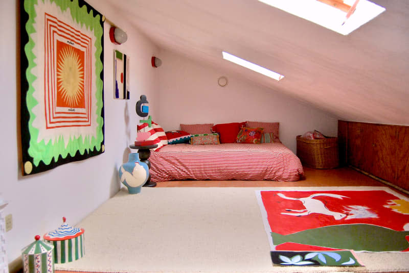 Colorful artwork on wall and floor of bedroom with bed with red striped bedding.