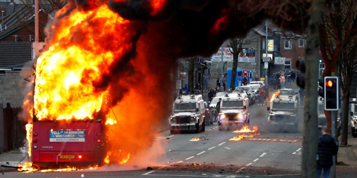 Police vehicles are seen behind a hijacked bus burns on the Shankill Road as protests continue in Belfast, Northern Ireland, April 7, 2021.
