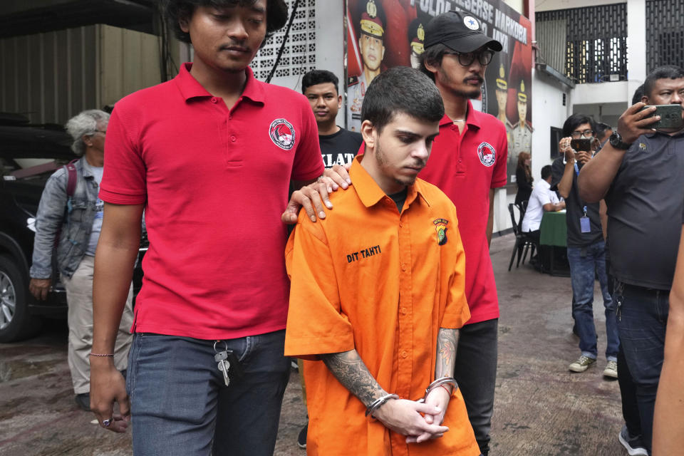 Plain-clothed police officers escort Brazilian national Gustavo Pinto da Silveira prior to a press conference at the regional police headquarters in Jakarta, Indonesia, Wednesday, March 15, 2023. Indonesian authorities said Wednesday they have arrested four foreigners who allegedly tried to smuggle drugs into the country's capital, including da Silveira who was caught with 2 liters (67.6 ounces) of liquid cocaine while arriving from Rio de Janeiro in January, and a Nigerian man who had swallowed dozens of capsules filled with more than a kilogram (2.2 pounds) of methamphetamine. (AP Photo/Tatan Syuflana)