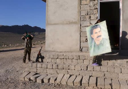 A female Kurdistan Workers Party (PKK) fighter adjusts her scarf while another carries a picture of jailed Kurdish militant leader Abdullah Ocalan at their base in Sinjar March 11, 2015. REUTERS/Asmaa Waguih