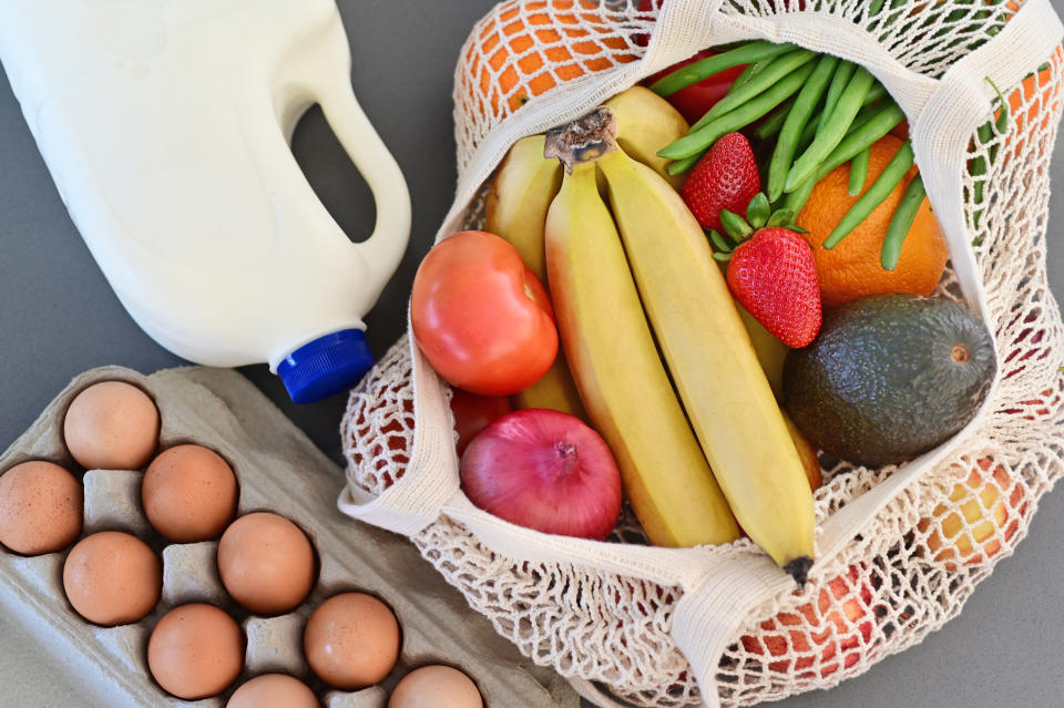 A shopping bag full of fresh vegetables and fruits, with milk and eggs on home kitchen counter.