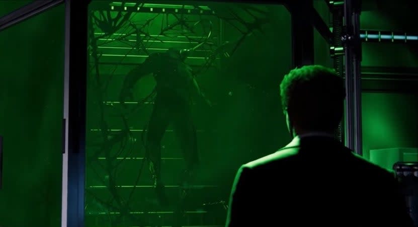 Harry Osborn floating in a green tank with the Venom symbiote attached to him with his father, Norman, watching him, in "Marvel's Spider-Man"