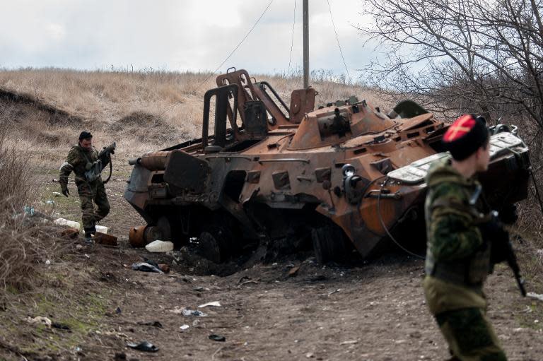 Pro-Russian rebels walk past a destroyed armoured vehicle in the Ukrainian city of Metalist, on March 23, 2015