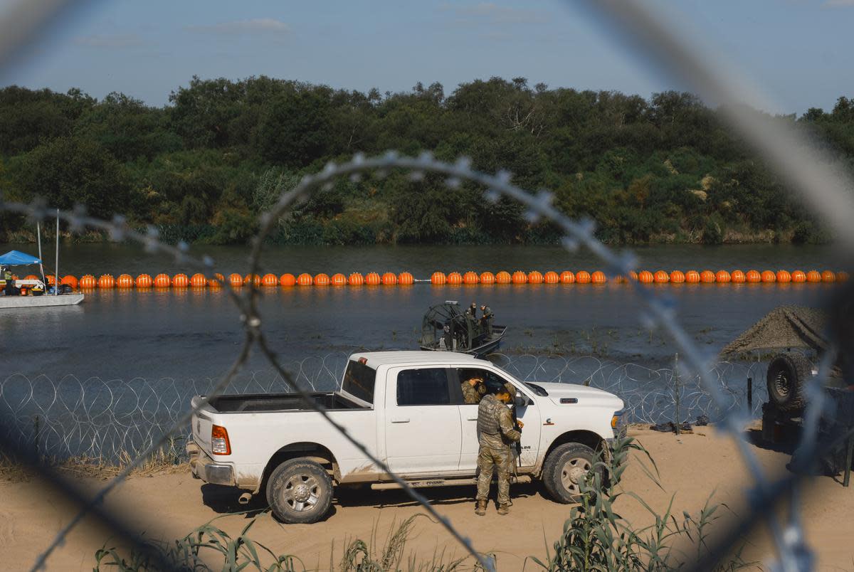 State law enforcement officers stand guard as workers construct a string of buoys which is being deployed to prevent migrants from swimming across the Rio Grande in Eagle Pass on July 14, 2023.