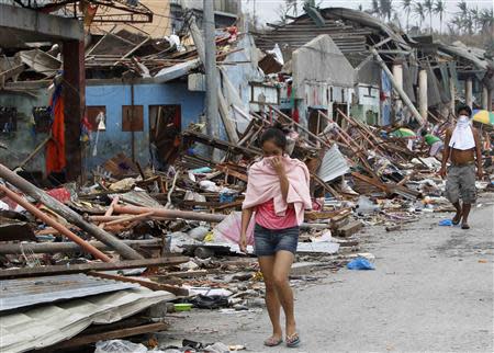 Residents cover their noses as they walk past devastated houses after super typhoon Haiyan hit Tacloban