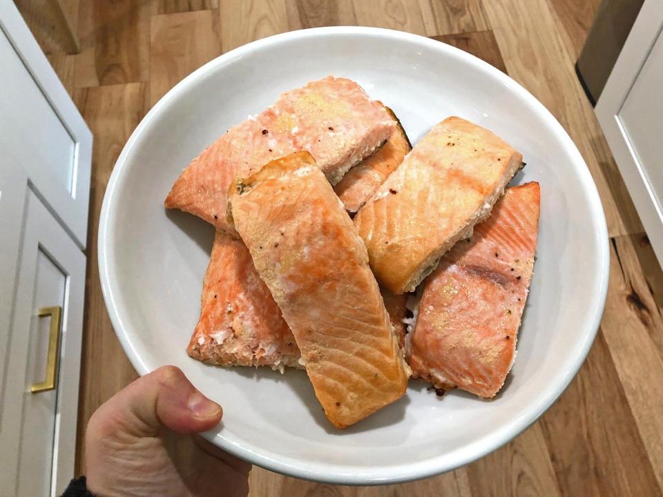 A hand holding a white bowl filled with salmon.