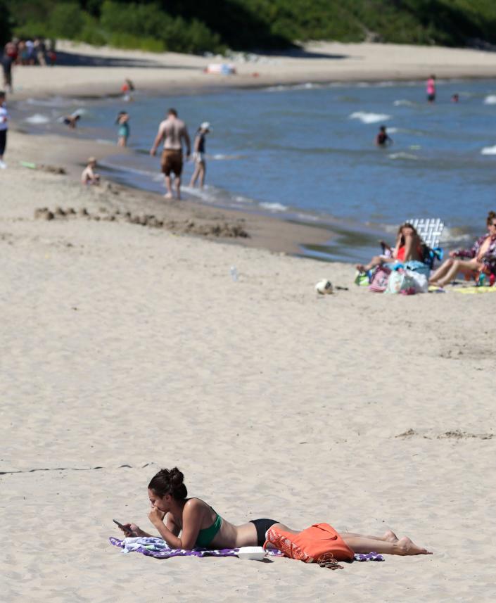 A young woman checks over her cell phone while getting some beach time in at Deland Park, Saturday, July 9, 2022, in Sheboygan, Wis.