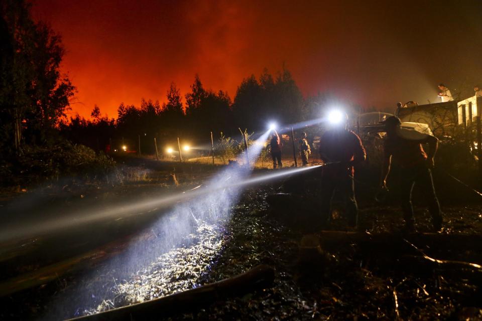 In this Sunday, Jan. 29, 2017 photo, a resident wets down the ground surrounding his home, threatened by a nearby wildfire in Portezuelo, Chile. Residents of some communities have been battling the fires themselves, without any protective gear and often using just branches or bottles of water in a frantic effort to save their homes, pasture and livestock. But those efforts are often undone as winds or smoldering ash spread the fires anew. (AP Photo/Esteban Felix)