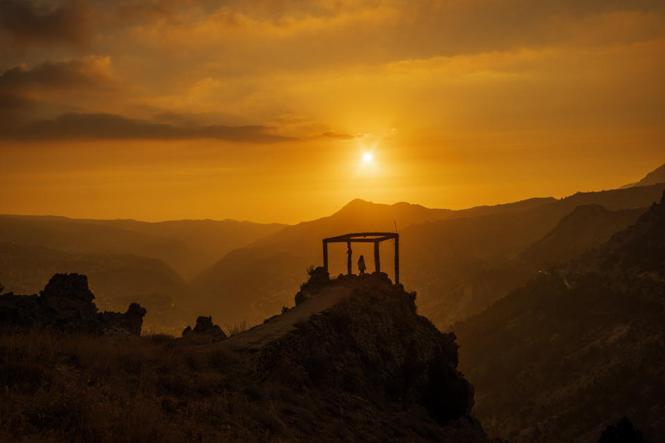 A girl watches the sunset over the scenic Kadisha Valley, a holy landmark for Lebanon's Maronite Christians, in the northeast mountain town of Bcharre, Lebanon, Friday, July 21, 2023. For Lebanon's Christians, the cedars are sacred, these tough evergreen trees that survive the mountain's harsh snowy winters. They point out with pride that Lebanon's cedars are mentioned 103 times in the Bible. (AP Photo/Hassan Ammar)