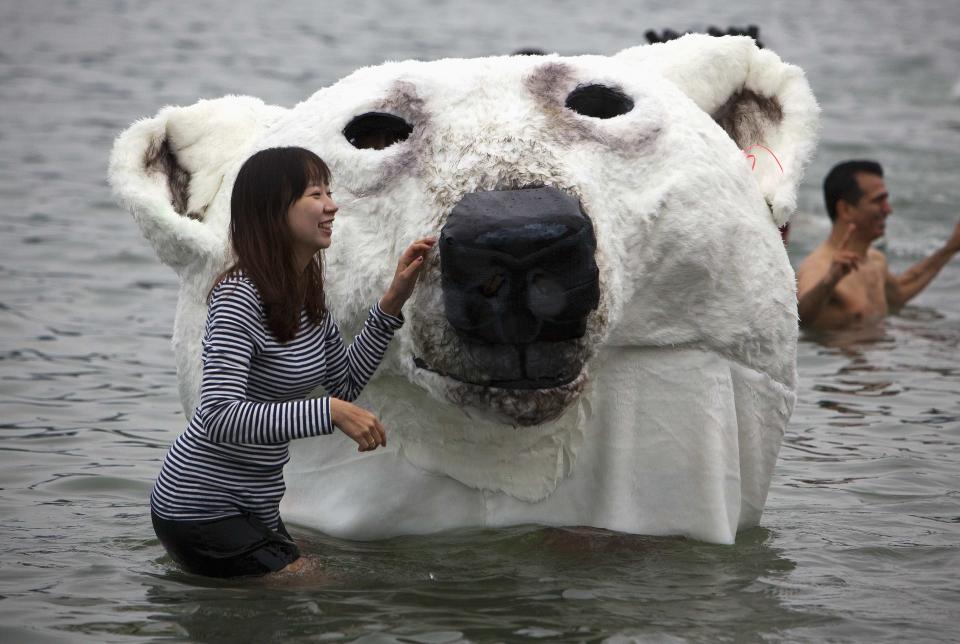 People pose next to a polar bear costume worn by two participants while running into English Bay during the 94th annual New Year's Day Polar Bear Swim in Vancouver