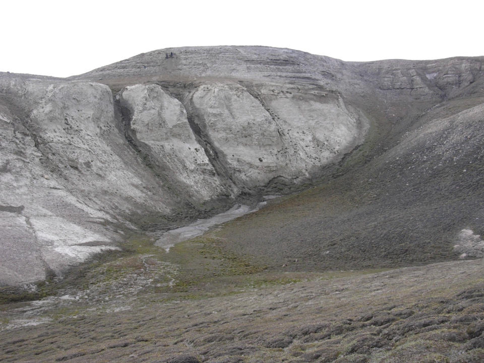 This 2006 photo provided by researchers shows geological formations at Kap Kobenhavn, Greenland. At the bottom of the section, the deep marine deposits are overlain by the coastal deposits of fine sandy material. The two people at the top are sampling for environmental DNA. Scientists have analyzed 2-million-year-old DNA extracted from dirt samples in the area, revealing an ancient ecosystem unlike anything seen on Earth today, including traces of mastodons and horseshoe crabs roaming the Arctic. (Svend Funder via AP)
