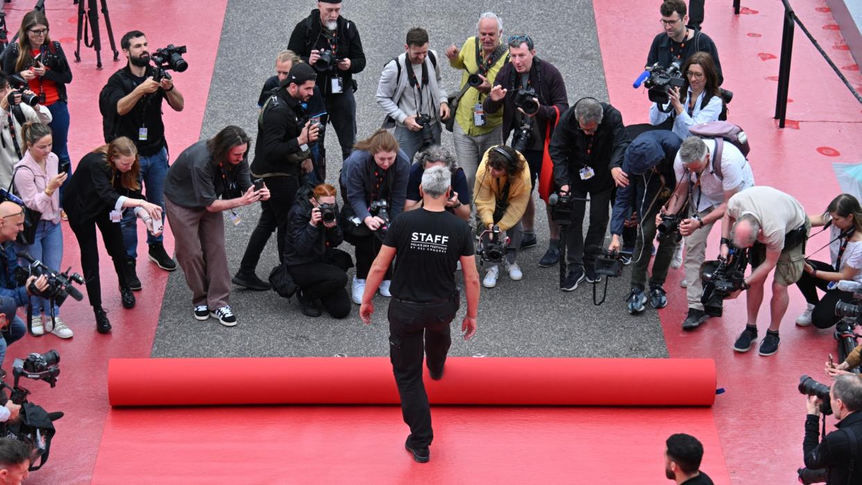  An employee rolls out the red carpet outside the Palais des Festivals in Cannes, while photographers take pictures. 