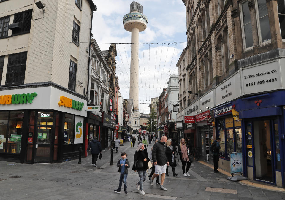 People stroll along a shopping street as new measures across the region are set to come into force in Liverpool, England, Wednesday, Oct. 14, 2020. New plans unveiled this week show Liverpool is in the highest-risk category, and its pubs, gyms and betting shops have been shut.(AP Photo/Frank Augstein)
