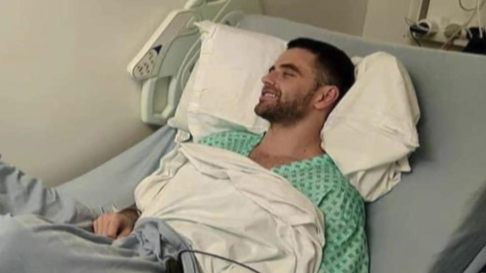 Jarryd Nurden sitting in a green hospital gown in a bed