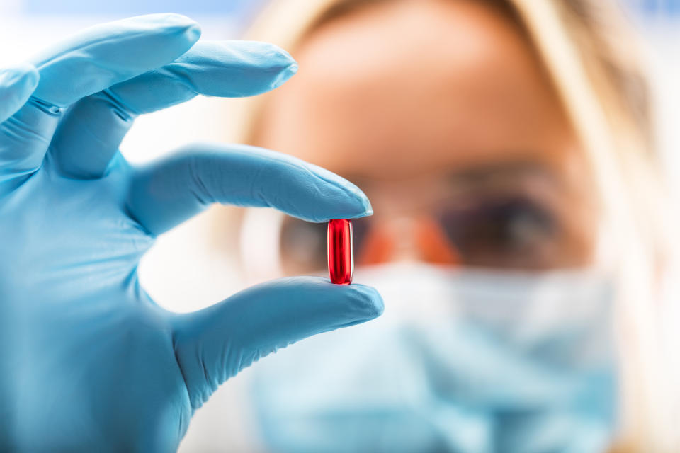Scientist holding up a red pill in front of her while wearing gloves