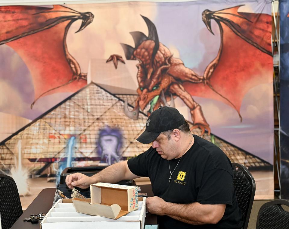 TJ Cafe & Games employee David "Flip" Defilippo sorts football cards in front of a poster of a dragon at the Milford gaming cafe, Jan. 12, 2021.   